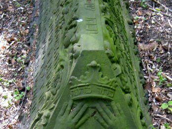 Tombstone in the shape of a triangular prism with carving of open book on short end with Hebrew and Portuguese inscriptions and decoration along length of stone. 