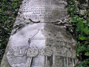 Gravestone of Esther de la Pena Gabay Henriques Tombstone flat on ground depicting coat of arms above Spanish inscription and relief of house surrounded by trees and next to sailboat.