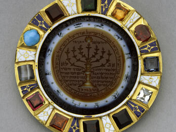 Amulet Circular amulet with stones around perimeter and image of candelabrum with Hebrew text in center, surrounded by images of the zodiac.