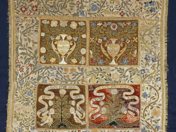 Torah Cover (?) Cloth embroidered with floral border, and four central panels, the top two with pitchers, vines, and flowers, and the bottom two with trees and ribbons with Hebrew text.