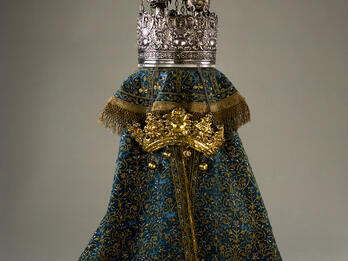 Torah Mantle Cloth cover with embroidery and metal crown, and crown resting on top of cloth.