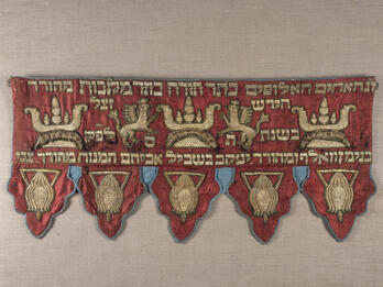 Short curtain embroidered with Hebrew text across the top with griffins and crowns. 