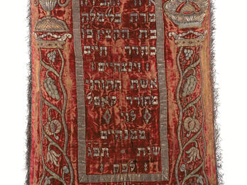 Torah Mantle Cloth with fringe on bottom, Hebrew text on top and middle, and border of foliage.