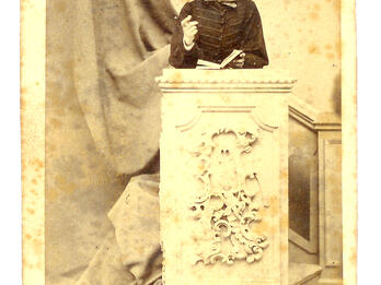 Photograph of young man wearing a hat and standing behind a podium.