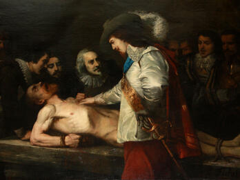 Painting of well-dressed man in hat with plume and sword putting his hand on the chest of a nude man tied down prone on a table with face upturned and mouth open, as several well-dressed men look on from the far side of the table. 