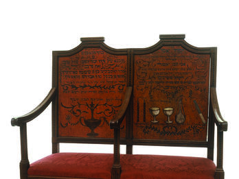 Two-seater bench with central armrest, decorated on the seat backs with ritual objects and Hebrew text.