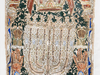 Papercut featuring Hebrew text, menorah in center, and crown at top. 