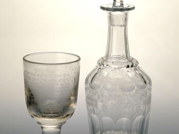 Kiddush Cup and Wine Carafe Glass cup and carafe with designs and Hebrew text etched on the outside.