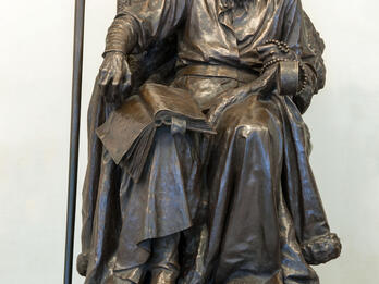 A sculpture of man with book and beads seated on throne.