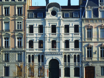 Photography of street view of buildings with low stone wall in front. 