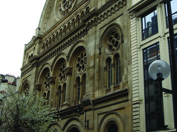 Photograph of exterior facade of building with arched doorways and circular windows. 