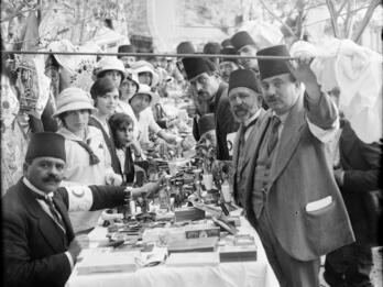 Photograph of women and men in fez hats sitting and standing at a long set table.
