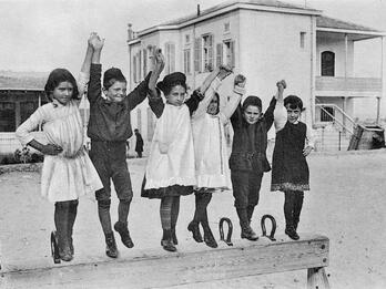 Students on a Pommel Horse Girls and boys holding hands and jumping on a pommel horse in front of a building.