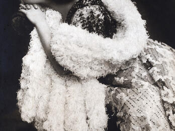 Photograph of woman in boa sitting on chair and looking to the side.