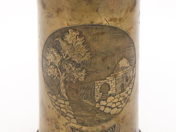 Ornamental Artillery Shell Casing Cylinder with etching of stone building along street, with Hebrew and English text in ribbons on bottom.