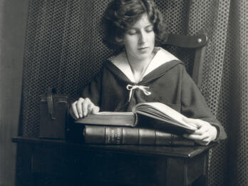 L'Image de la femme (The Image of Woman) Photograph of figure seated at desk reading a book.