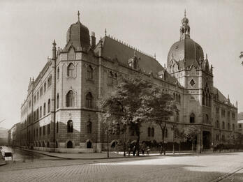 Photograph of brick building on street corner with ornate roof finials and domed roofs.