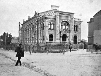 Lazar Brodsky Choral Synagogue Photograph of exterior of building with rounded window frames and decorative columns, and man in hat walking toward it.