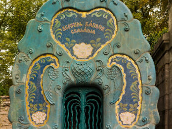 Photograph of gated door outside, surrounded by large archway and decorative floral motifs.