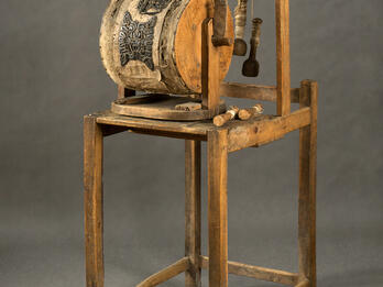 Wooden machine on four legs, with barrel and handle in center.