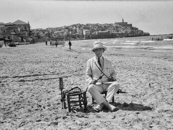 Self-Portrait on Tel Aviv Beach Photograph of man sitting on beach in hat and suit with hookah pipe in hand.