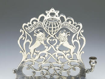 Eight-branched candelabrum with backplate with lions, a Hebrew inscription, Stars of David, and a scalloped top edge. 