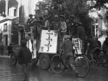 Billboards for Municipal Elections, Tel Aviv Photograph of men huddled together on a car holding billboards, surrounded by young men on bicycles following them down the street.