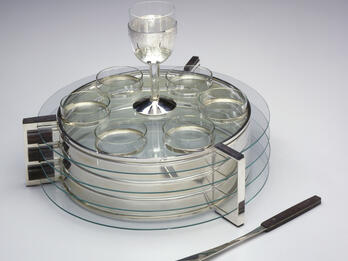 Circular platter with three glass tiers joined by vertical mounts, and wine cup and six small bowls on top. 