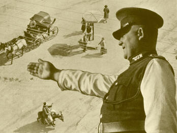 Photograph of policeman towering over a street with horse-drawn wagon, several people, and person on donkey.