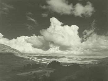 Photograph of valley with buildings under cloudy sky.