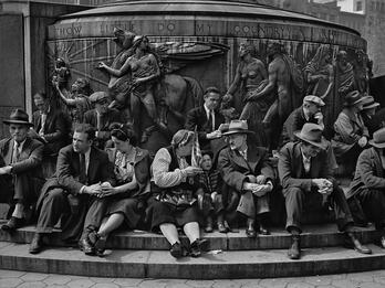 May Day, Union Square, New York City Photograph of men, women, and children seated on the steps of a large public monument with nude classical figures and a winged horse atop a circular base.