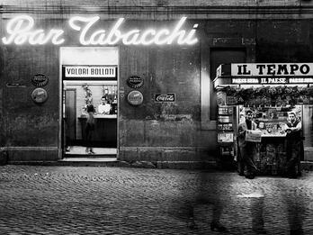 Photograph of building from street featuring neon sign and two storefronts.