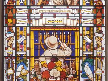 Stained-Glass Window, Central Synagogue, Portland Street, London Stained glass window featuring a man in the center facing away from viewer lighting a menorah behind a table set for Shabbat, a rabbi above him next to a harp, and biblical images and Hebrew words, flowers, birds, and other objects.