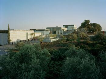 Photograph of several low buildings on a hill surrounded by trees.