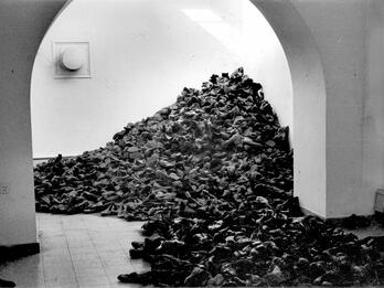 Art installation of large number of boots piled between two rooms.