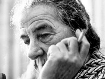 Photograph of an elderly woman smoking a cigarette, whose face is partially blocked by her hand holding the cigarette. 