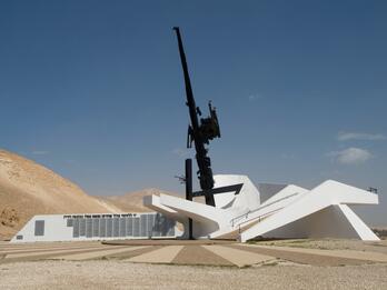 Jordan Valley Memorial Monument Cement and steel monument resembling a large firearm in a white base next to a building, surrounded by sand dunes.