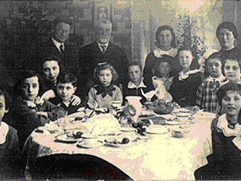 The Birthday Party Photograph of many people sitting around a set table and looking at the camera.