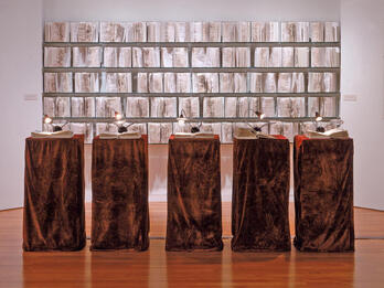 The Liberation of G-d Installation featuring five podiums with an open book and reading light on top of each with open books on the wall behind.