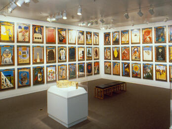 The Chapter Paintings Installation photograph featuring walls of paintings and jewel case and bench in center of room.