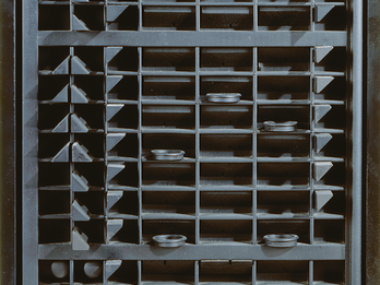 Abstract painted wood sculpture of a rectangle with a grid of small squares and rectangles inside containing triangles and circles.