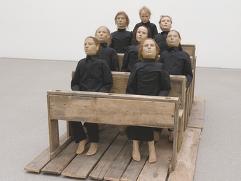 Art installation of eight figures sitting on pews. 