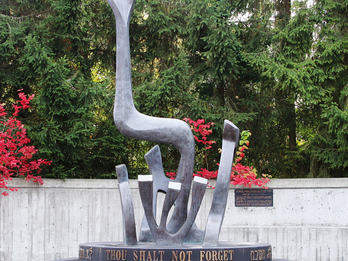 Sculpture in the shape of Hebrew letters, with a circular base with English and Hebrew words, set against a leafy backdrop. 