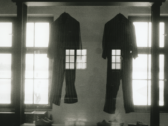 Dachau, 1985 Photograph depicting two jumpsuits hanging between two large windows superimposed over an image of a human figure standing with their back turned.