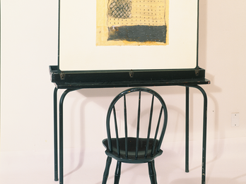 Sculpture of empty chair at desk that holds up a painting resembling a flag.