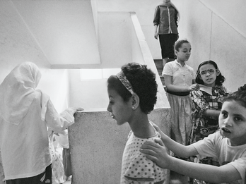 Blind Women, Egypt Photograph featuring four young girls holding onto each other's shoulders walking down the stairs in a train with two older women in the front and back.