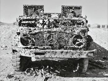 Photograph of bullet-riddled truck in desert. 