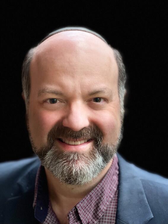 A bearded man wearing a kippah smiles into the camera.