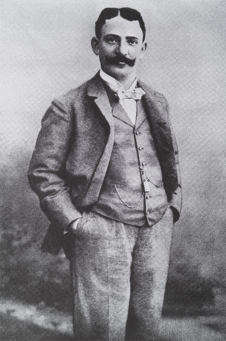 Photograph of man standing with hands in his pockets.