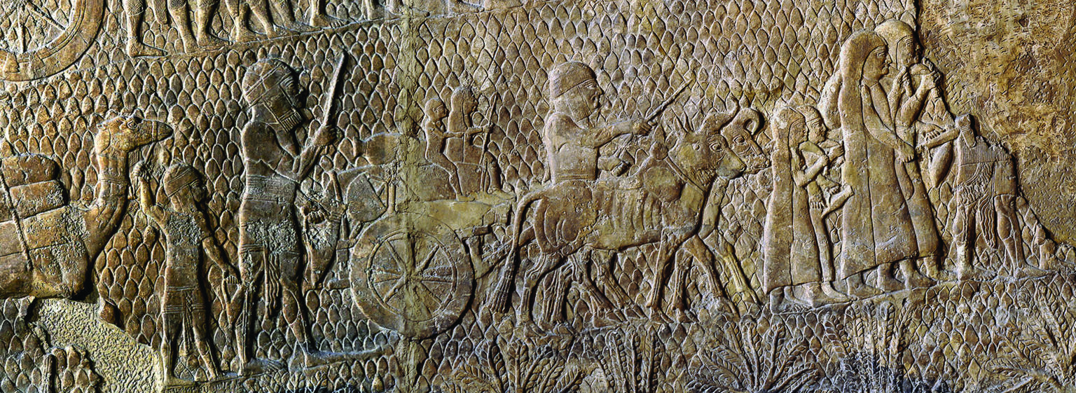 Wall relief depicting profile view of barefoot captives walking with camels, bulls, and wagons.